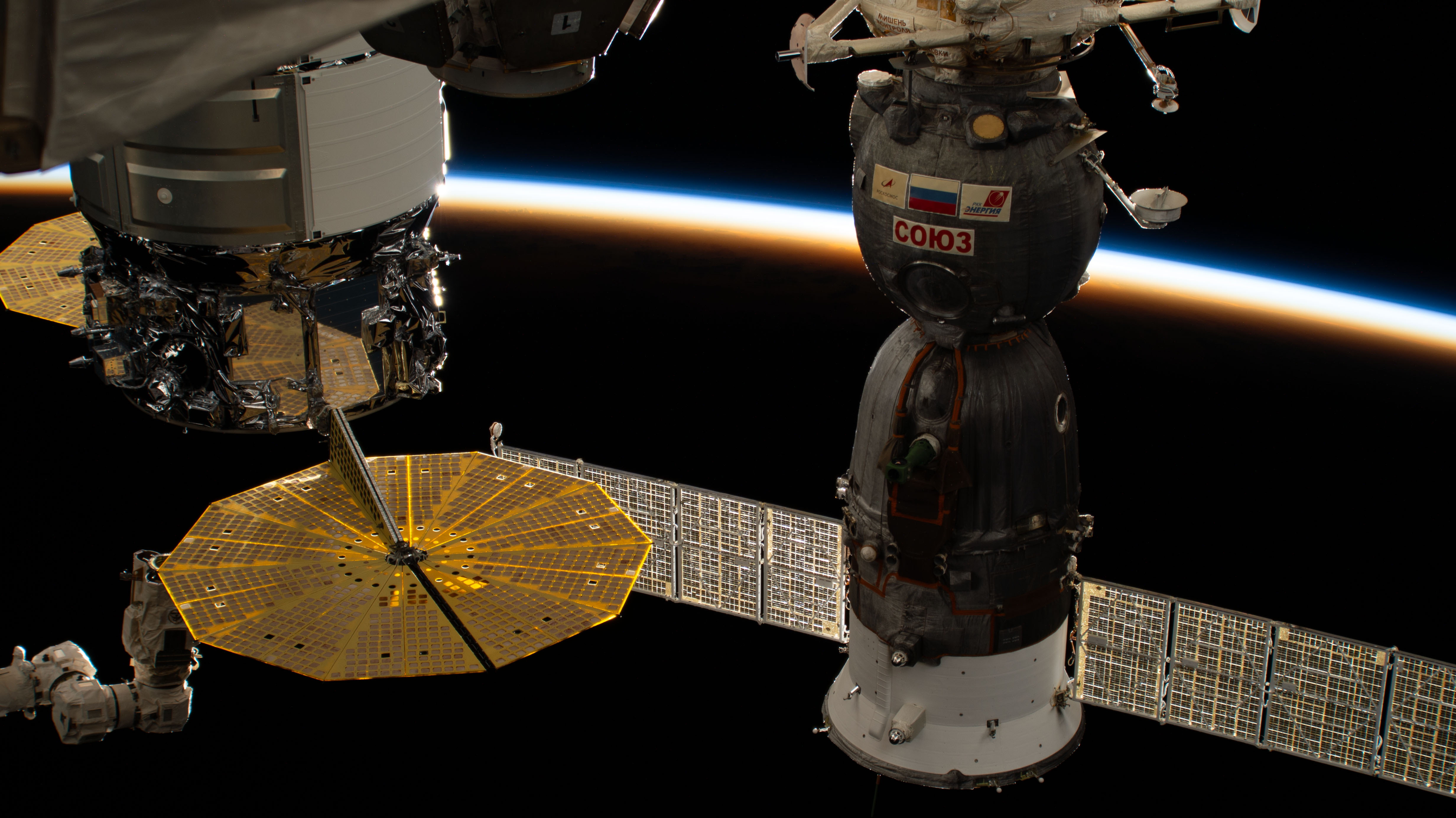 The last rays of an orbital sunset illuminate Earth's atmosphere in this photograph from the International Space Station as it orbited 259 miles above Central America. In the foreground from left are, Northrop Grumman's Cygnus resupply ship, with its prominent cymbal-shaped UltraFlex solar arrays, and the Soyuz MS-24 crew spacecraft.