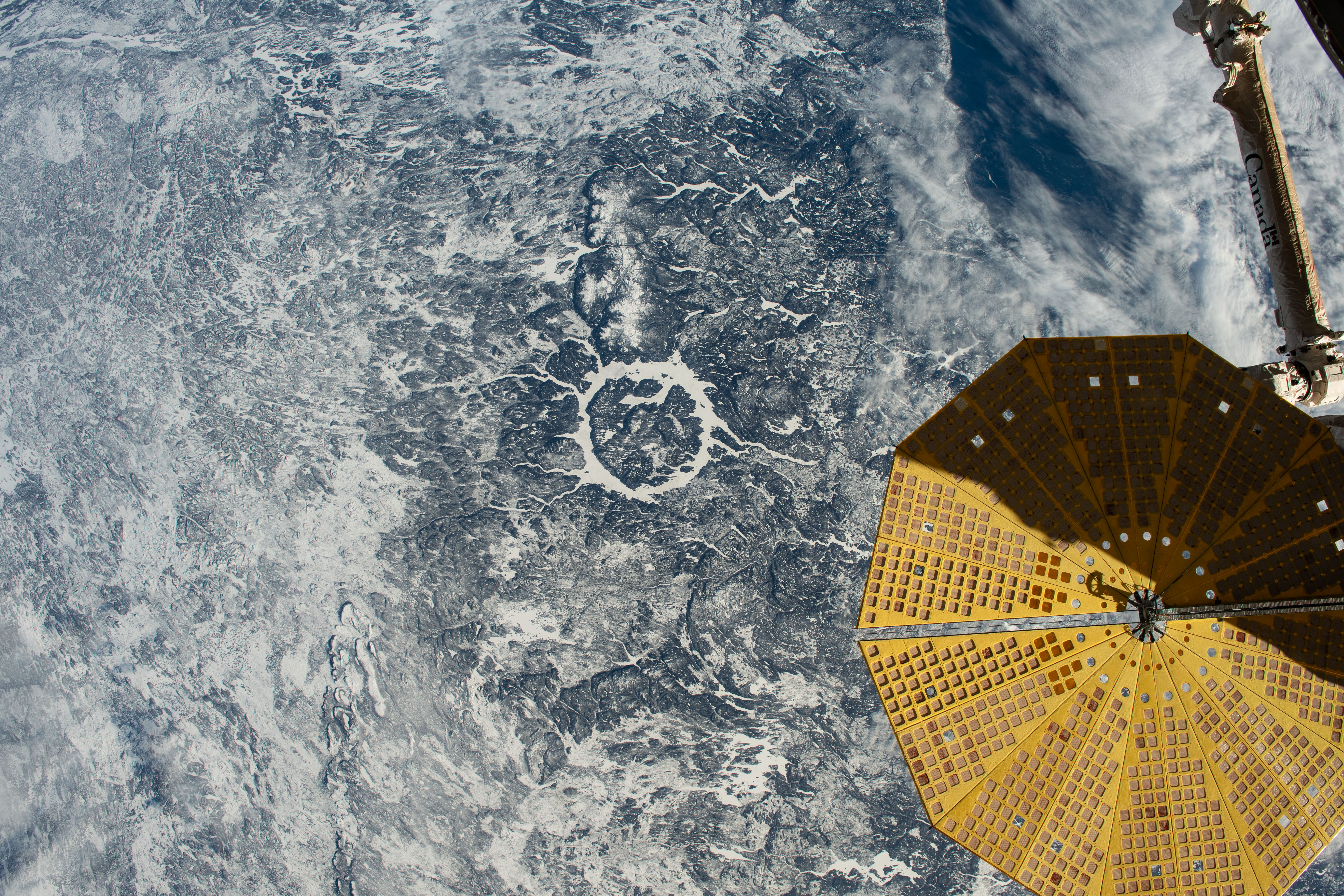 The Manicougan impact crater in Canada's province of Quebec, with the Cygnus space freighter's UltraFlex solar array in the lower right foreground, is clearly visible from the International Space Station as it orbited 264 miles above.
