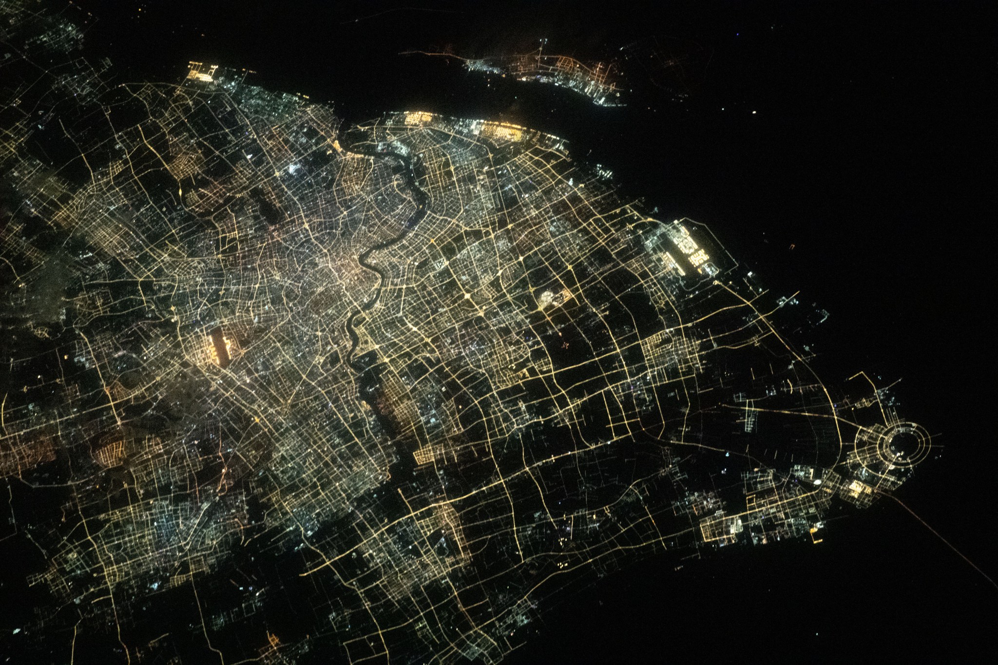 A night view of Shanghai from the International Space Station, 260 miles above Earth. The city's lights illuminate roads; the surrounding area is dark.
