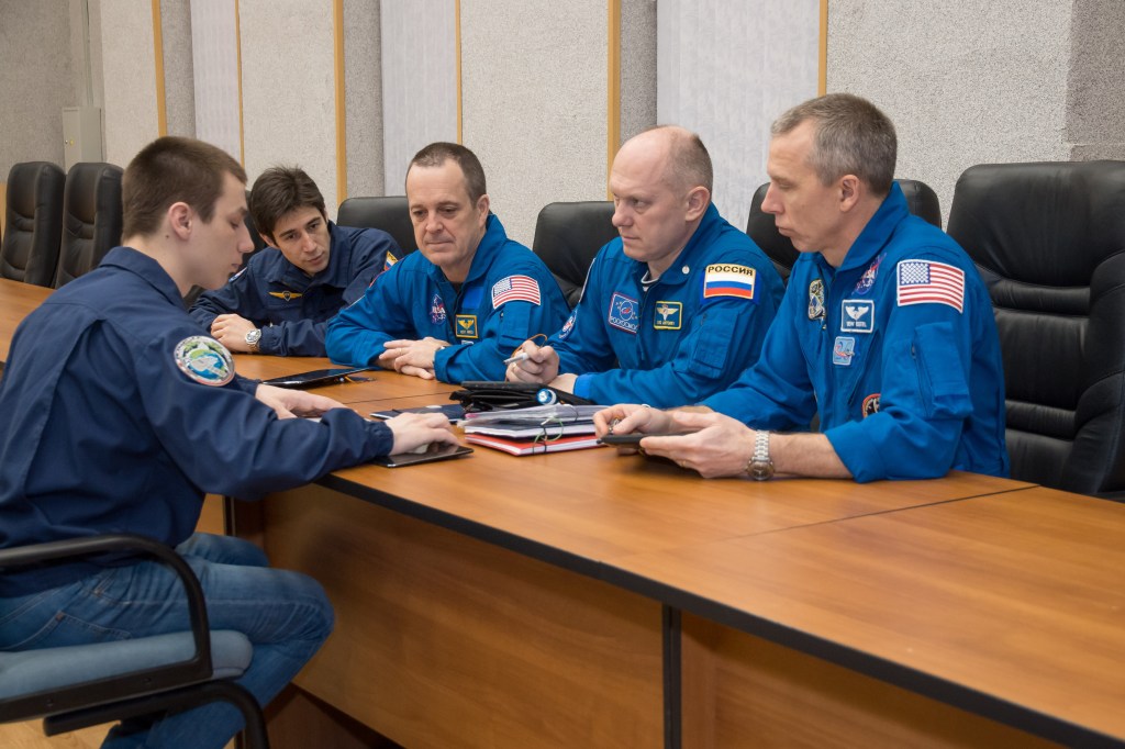 At the Cosmonaut Hotel crew quarters in Baikonur, Kazakhstan, Expedition 55 crew members Ricky Arnold of NASA (second from left), Oleg Artemyev of Roscosmos (second from right) and Drew Feustel of NASA (right) listen to training instructors March 15 as part of their pre-launch activities. They will launch March 21 on the Soyuz MS-08 spacecraft from the Baikonur Cosmodrome on a five-month mission to the International Space Station.
