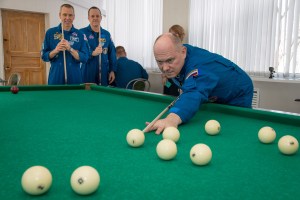 jsc2018e025552 - At the Cosmonaut Hotel crew quarters in Baikonur, Kazakhstan, Expedition 55 crew member Oleg Artemyev of Roscosmos tries his hand at billiards March 15 as his crewmates, Drew Feustel of NASA (left) and Ricky Arnold of NASA (right) look on. They will launch March 21 on the Soyuz MS-08 spacecraft from the Baikonur Cosmodrome on a five-month mission to the International Space Station.