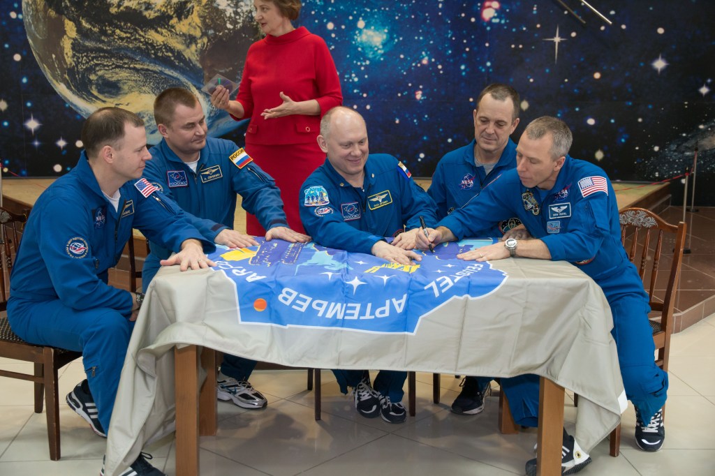 In the Korolev Museum at the Baikonur Cosmodrome in Kazakhstan, the Expedition 55 prime and backup crew members sign a flag bearing their Soyuz MS-08 crew patch insignia March 16 during a traditional preflight tour of the museum. From left to right are backup crewmembers Nick Hague of NASA and Alexey Ovchinin of Roscosmos and prime crewmembers Oleg Artemyev of Roscosmos, Ricky Arnold of NASA and Drew Feustel of NASA, who will launch March 21 on the Soyuz MS-08 spacecraft for a five-month mission on the International Space Station.