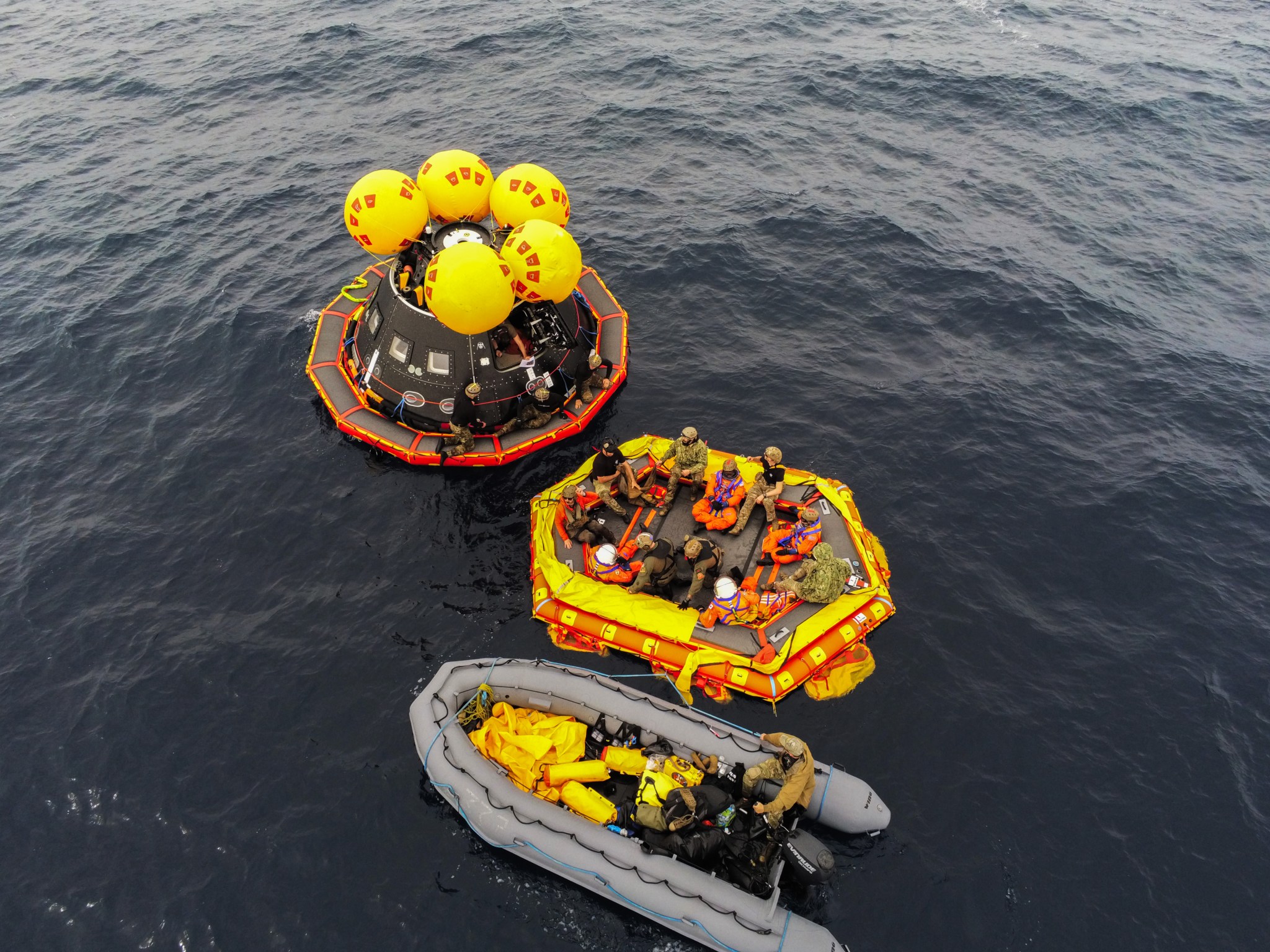 NASA's Artemis II crew members and U.S. Navy personnel exit a mockup of the Orion spacecraft onto an inflatable “front porch”