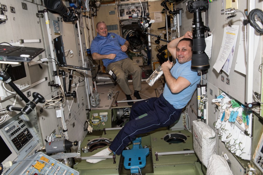 NASA astronaut Scott Tingle (background left) and Commander Anton Shkaplerov relax inside the Zvezda service module moments before the arrival of three new Expedition 55 crew members on March 23, 2018. The Soyuz MS-08 spacecraft carrying Soyuz Commander Oleg Artemyev and Flight Engineers Drew Feustel and Ricky Arnold would dock to the Poisk docking compartment on March 23, 2018 at 3:40 p.m. EDT.