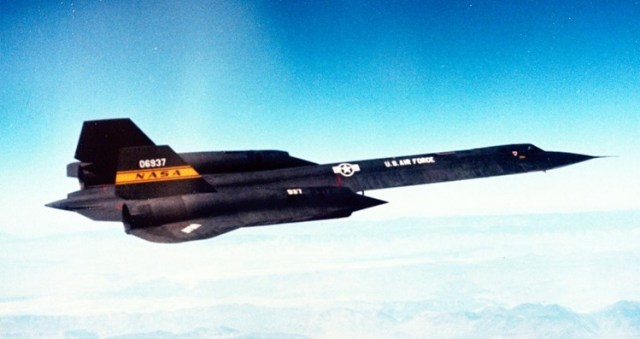 A black YF-12C aircraft with a white U.S. Air Force logo on the front section and an orange NASA logo on the tail flies above white clouds and a blue sky.