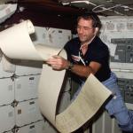Astronaut Richard H. Truly, STS-2 pilot, peruses some teleprinter copy, floating partially about the middeck area of NASA’s space shuttle Columbia during one of 1,813 minutes of activity of STS-2.