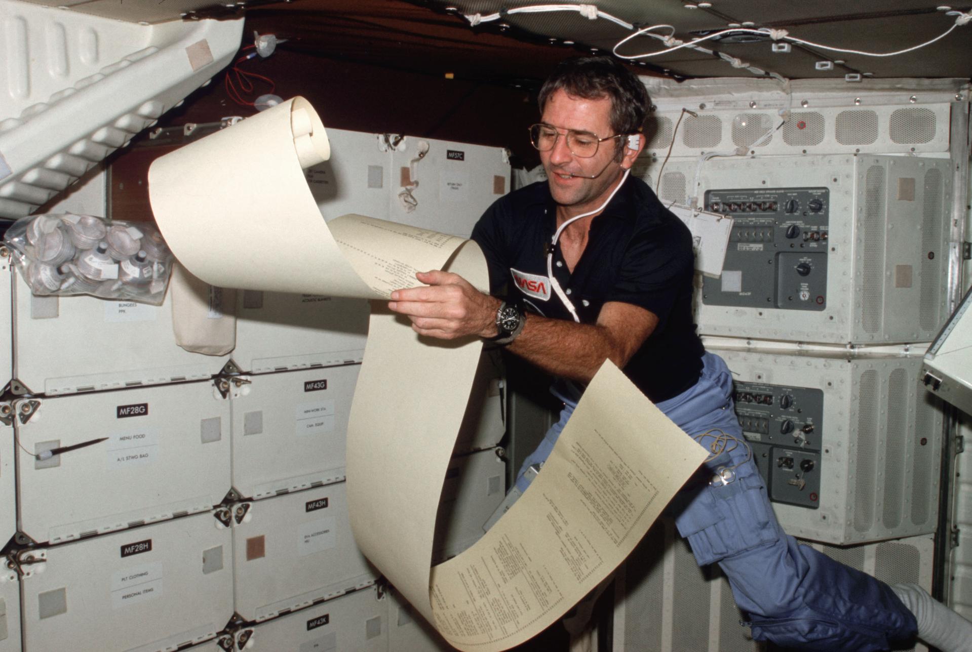 Astronaut Richard H. Truly, STS-2 pilot, peruses some teleprinter copy, floating partially about the middeck area of NASA’s space shuttle Columbia during one of 1,813 minutes of activity of STS-2.