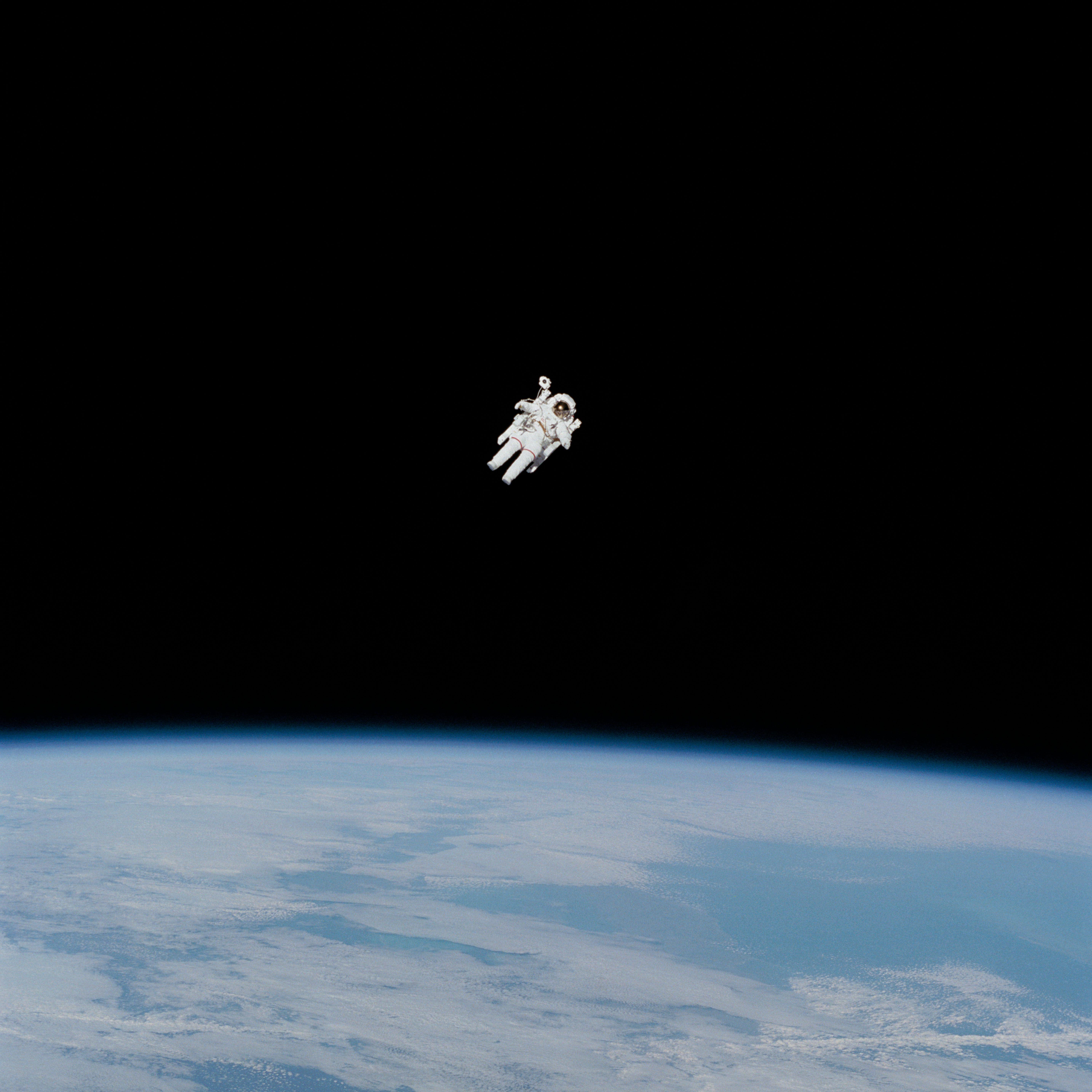 An astronaut is surrounded by empty space as he floats at a 45-degree angle above Earth.