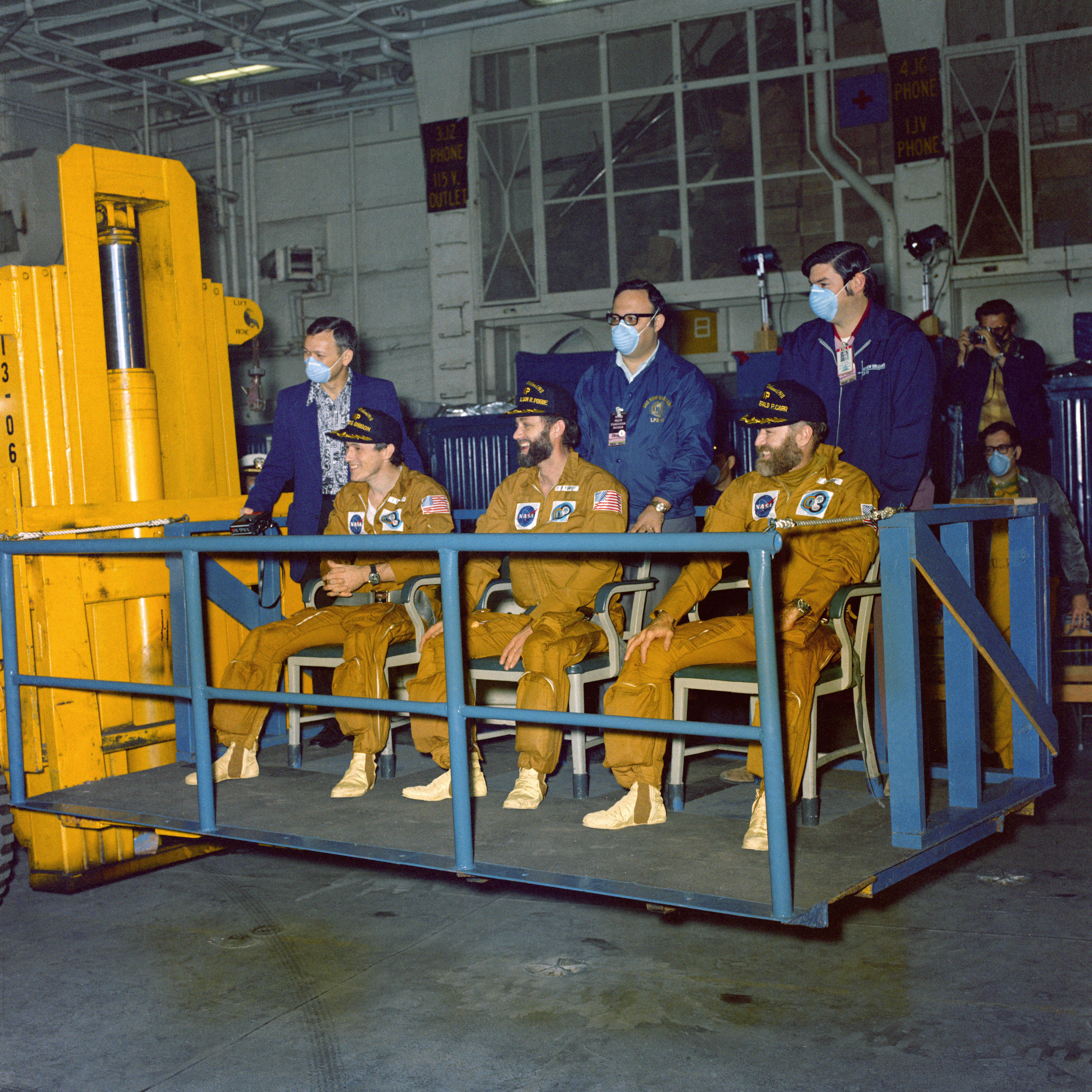 Skylab 4 crew members Gibson, left, Pogue, and Gerald P. Carr seated on a forklift platform after emerging from the CM and on their way to the medical facility