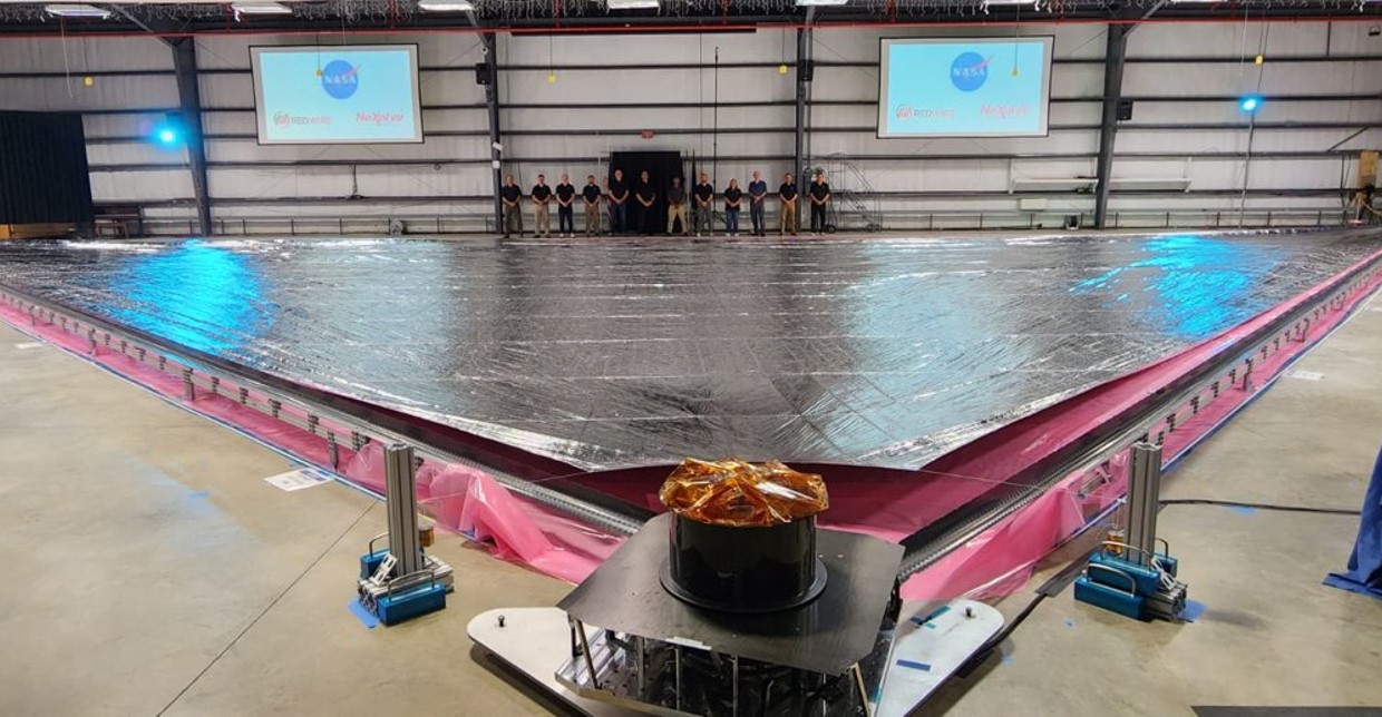 A group of employees stand in the back of a room filled with an expanded silver solar sail.