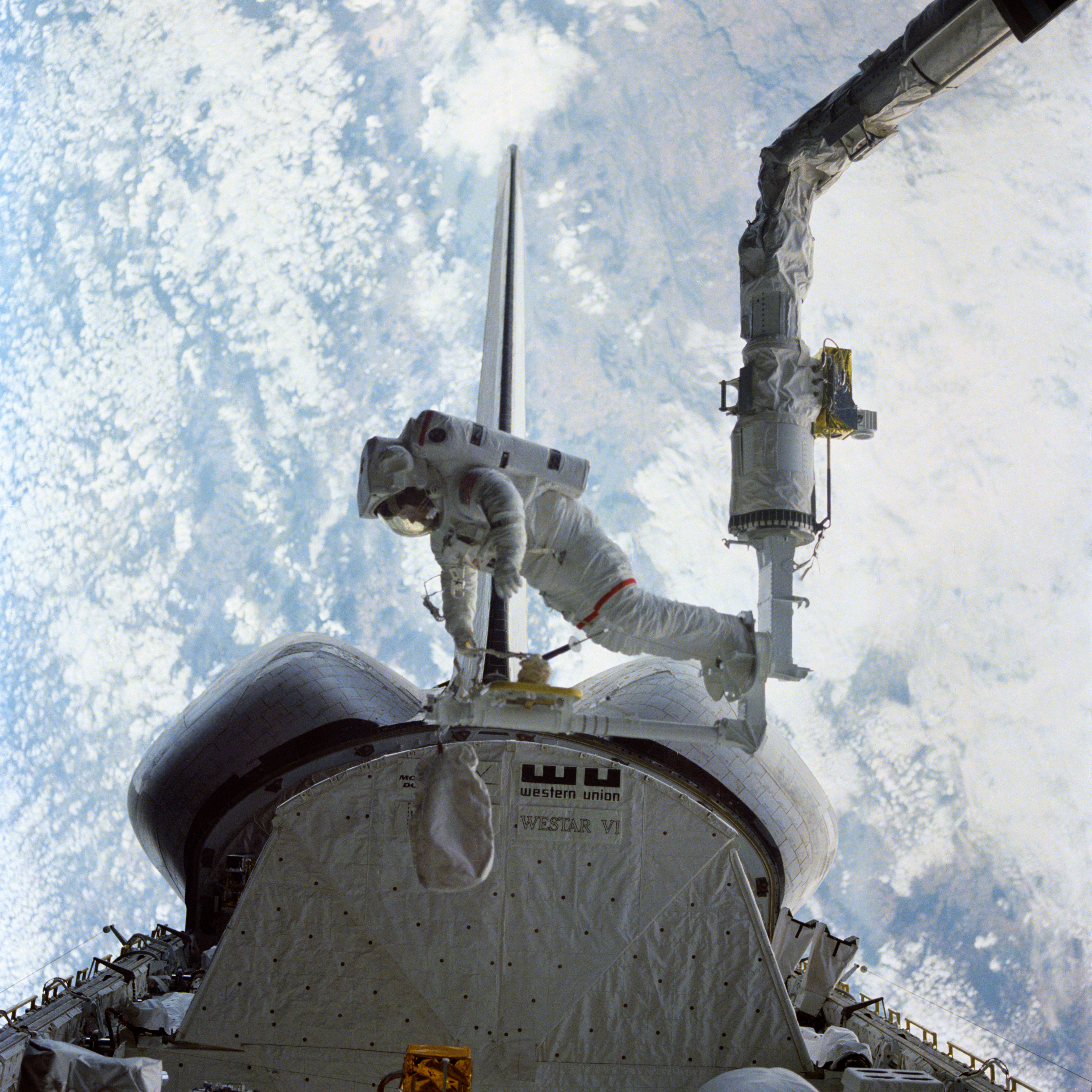 View of Bruce McCandless testing the Manipulator Foot Restraint at the end of the Remote Manipulator System, operated by Ronald E. McNair