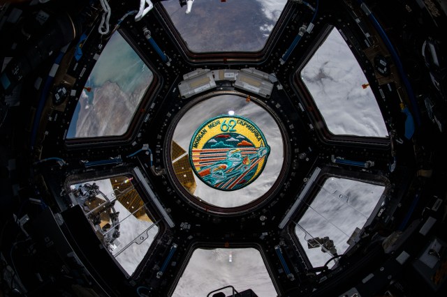iss062e038341 (Feb. 21, 2020) --- The Expedition 62 mission patch floats inside the seven-window cupola, the International Space Station's "window to the world." The orbiting complex was flying 265 miles above Russia near the Caspian Sea at the time this photograph was taken.