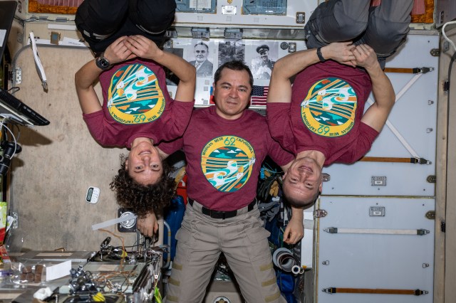 iss062e000449 (Feb. 7, 2020) --- The three-member Expedition 62 crew, sporting their mission patch on t-shirts, will be living aboard the International Space Station until April of this year. In the center, is Roscosmos Commander Oleg Skripochka flanked by NASA Flight Engineers Jessica Meir and Andrew Morgan.