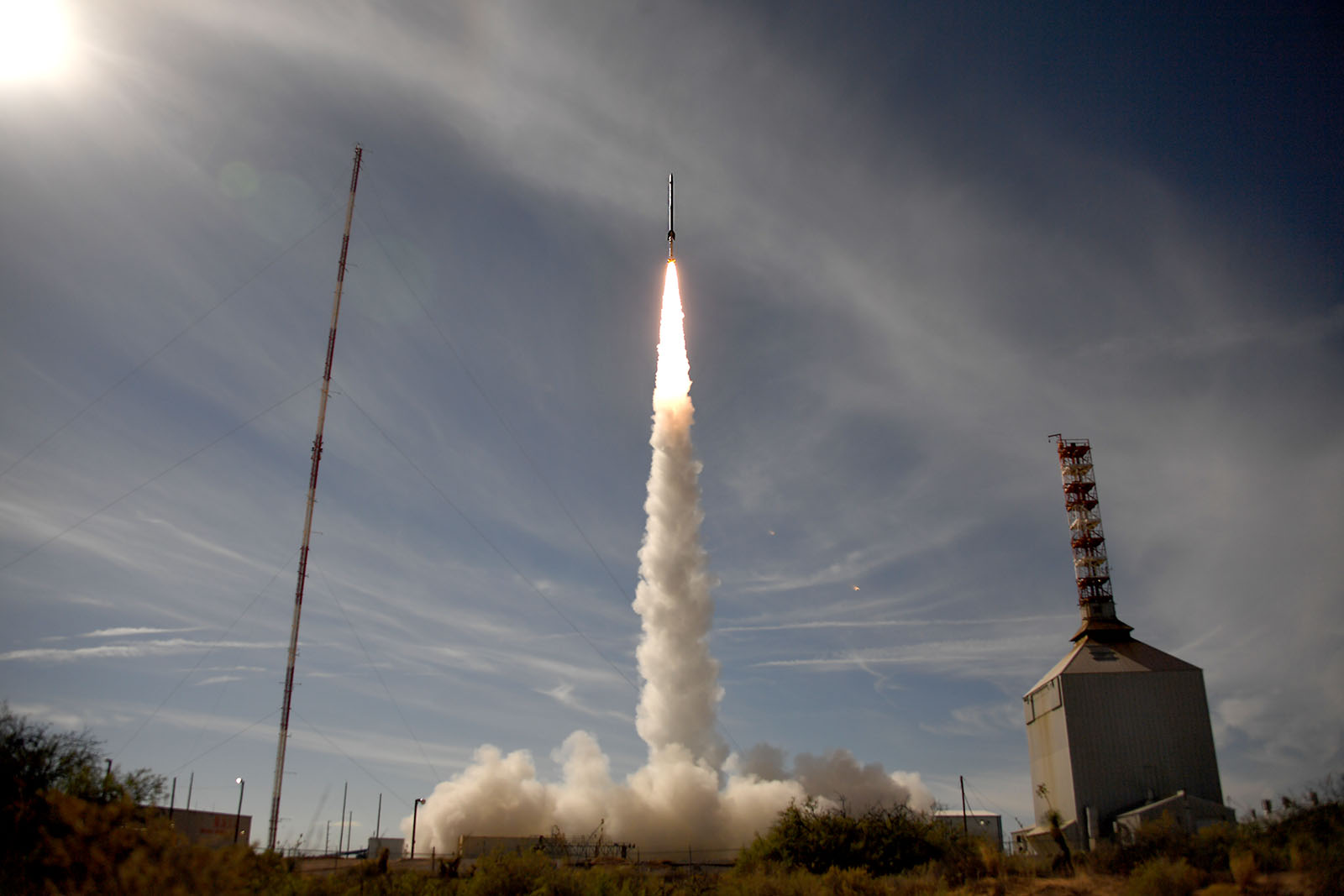 A wide shot of a sounding rocket just after lifting off from a launch pad, a trail of smoke underneath it.