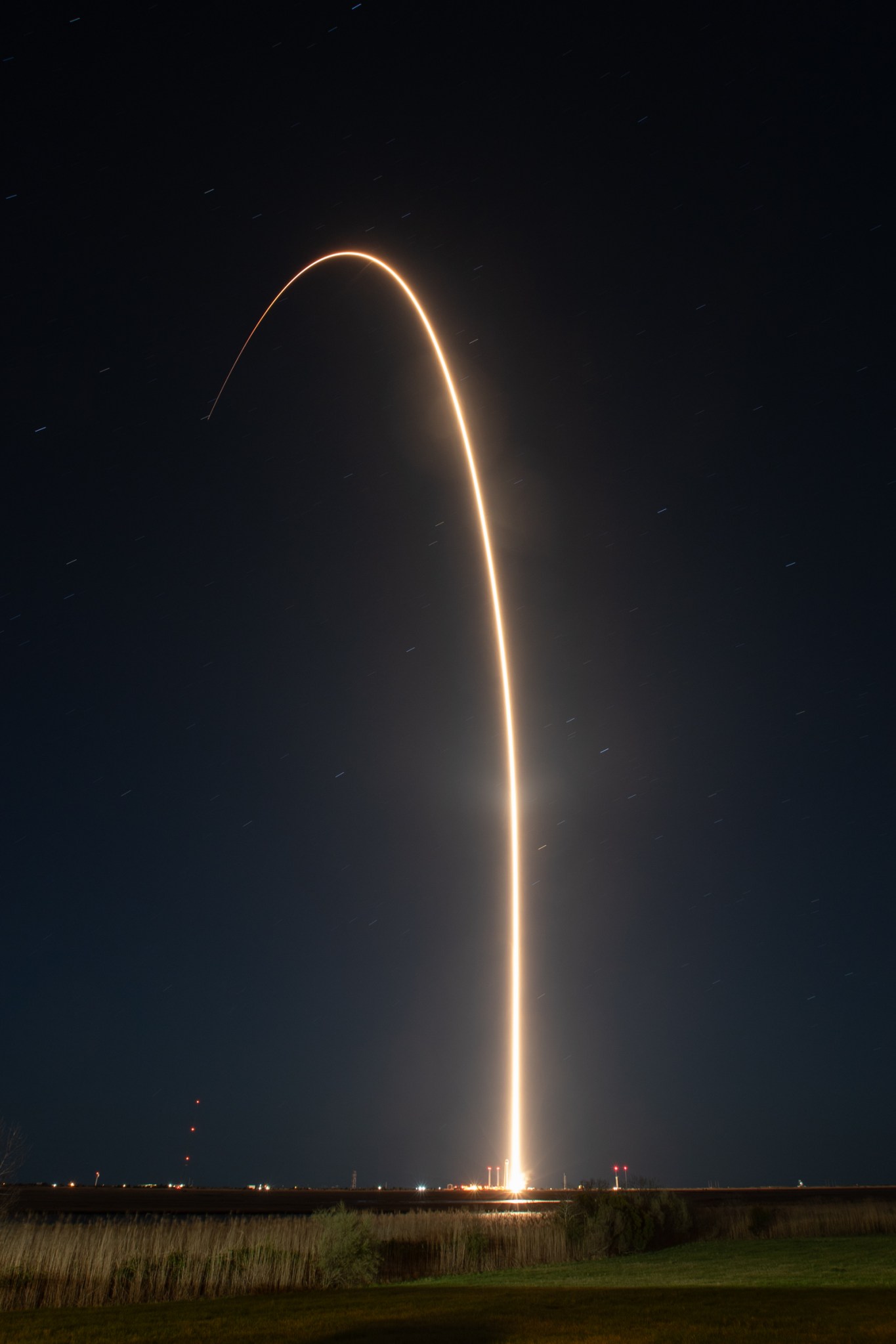 A long exposure photo of Rocket Lab's Electron launch, represented by a white streak moving from the center bottom curving slightly to the