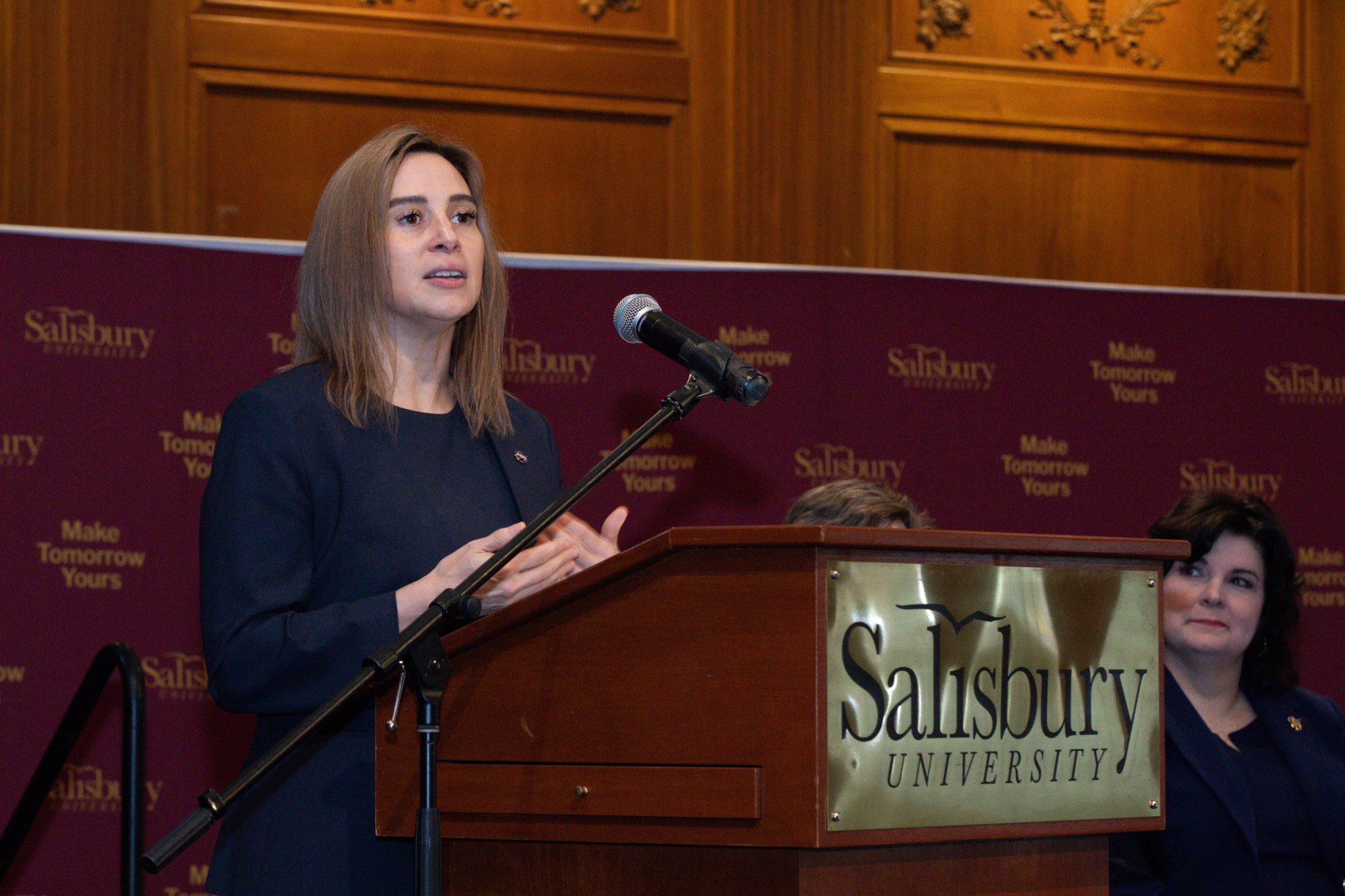 Dr. Makenzie Lystrup speaks at a podium. The words "Salisbury University" on a gold plaque on the front of the podium.
