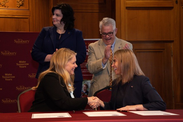 Dr. Makenzie Lystrup shakes hands Dr. Carolyn R. Lepre at a table, with Dr. Laurie Couch and Dave Pierce standing behind them.