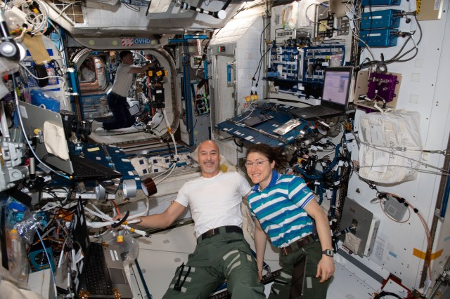 iss060e014372 (July 24, 2019) --- Astronauts Luca Parmitano and Christina Koch pose for a playful portrait inside the International Space Station's Harmony module. In the background, astronaut Nick Hague inspects and cleans fans and vents located in the U.S. Destiny laboratory module.