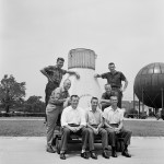 The Mercury 7 astronauts pose around a boilerplate capsule