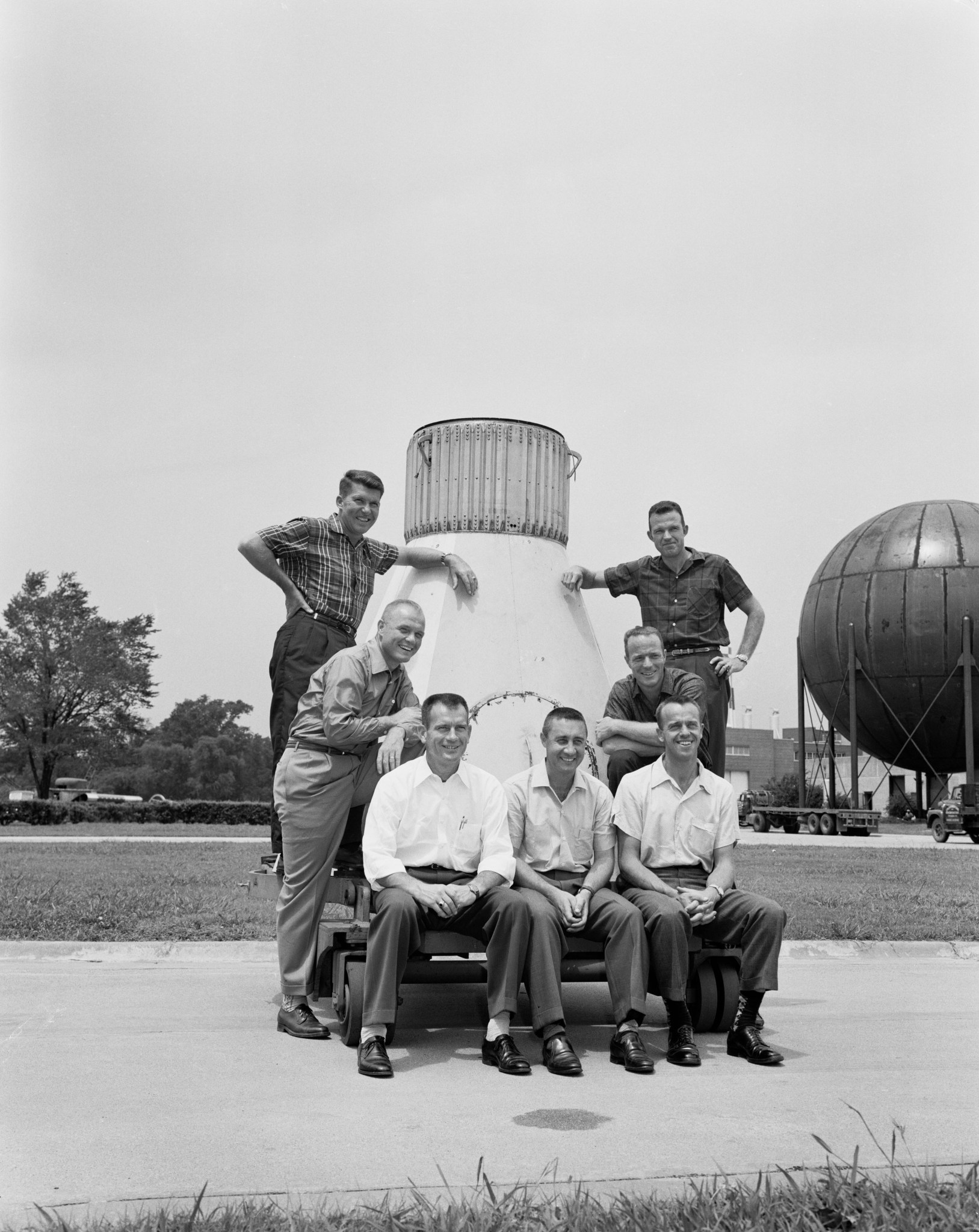 The Mercury 7 astronauts pose around a boilerplate capsule