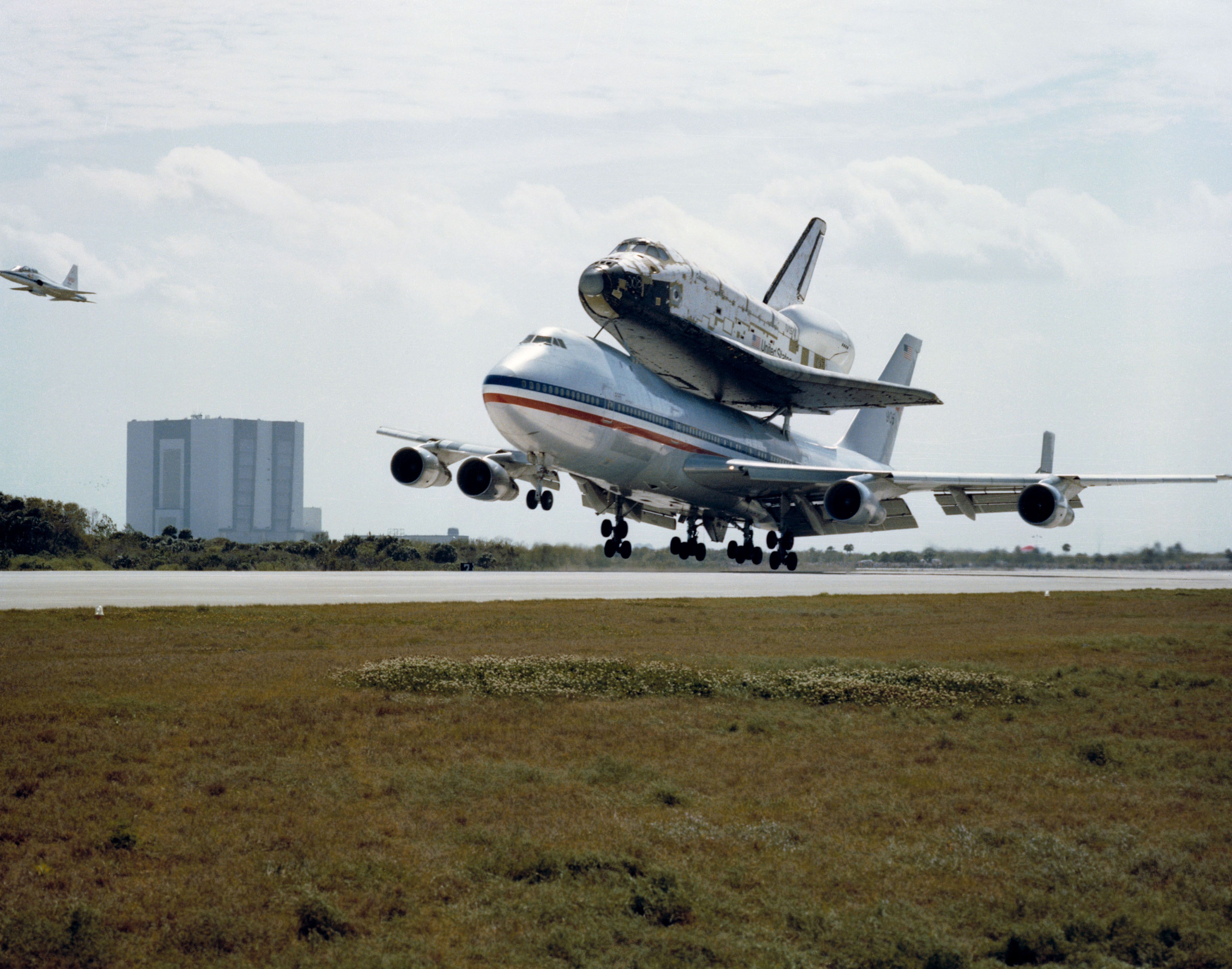 Columbia atop the SCA touches down at KSC’s Shuttle Landing Facility (SLF), with the Vehicle Assembly Building visible in the background