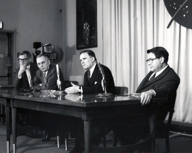 Four men setting at press conference table.