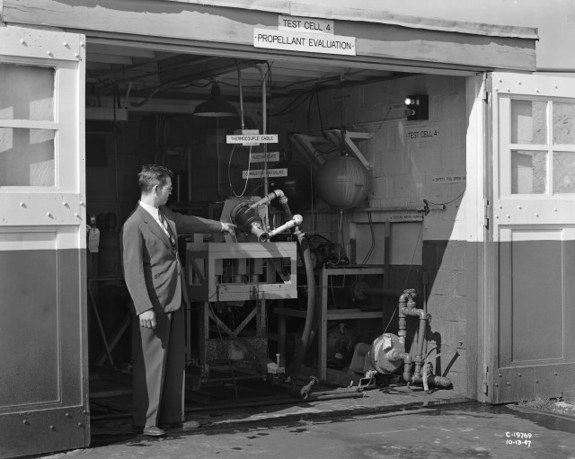 Man pointing at rocket engine in test cell.