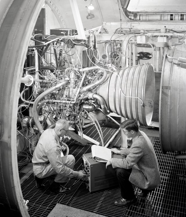 Two men with rocket engine in test chamber.