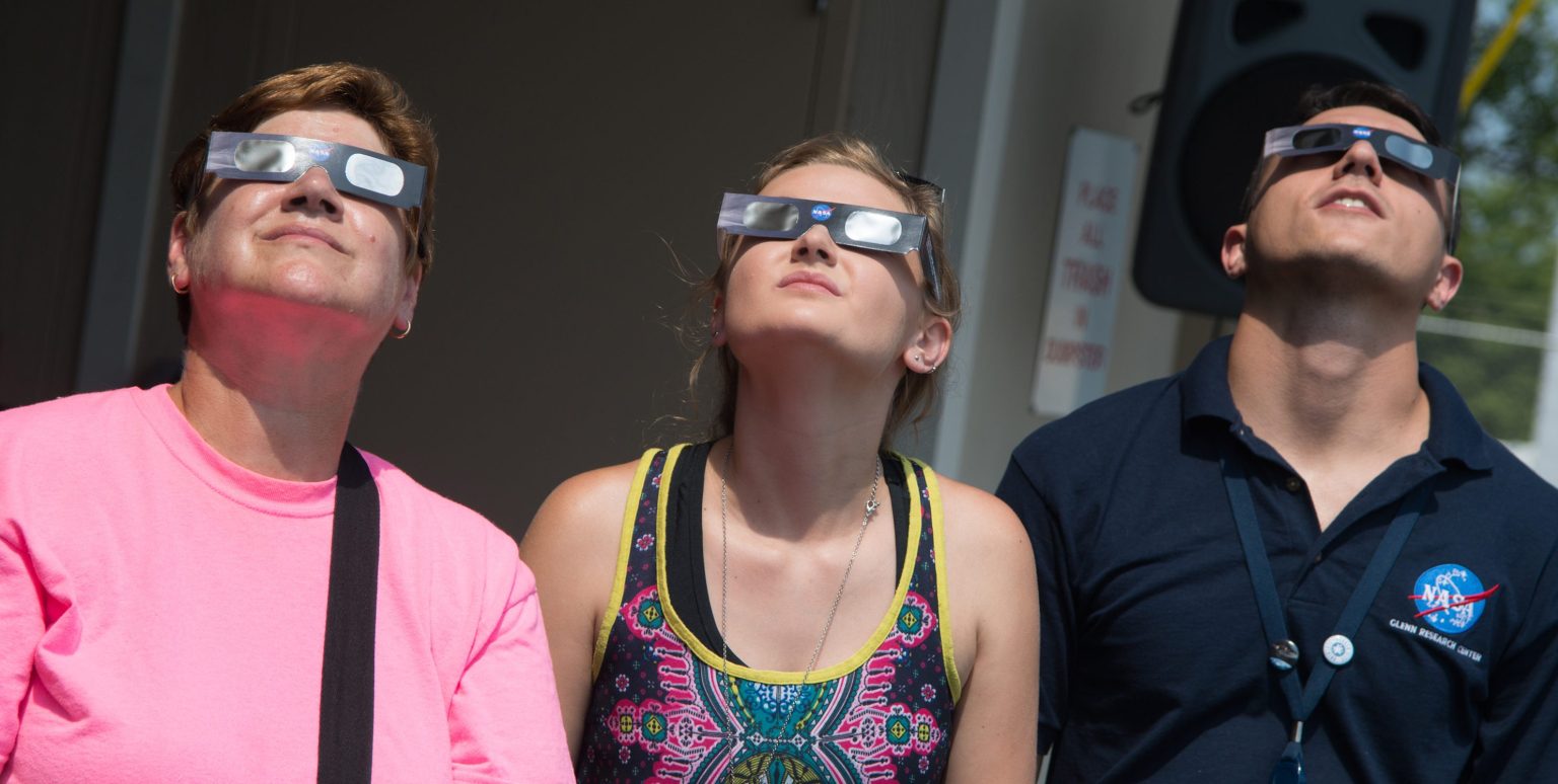 People wearing eclipse glasses look up at the sun.