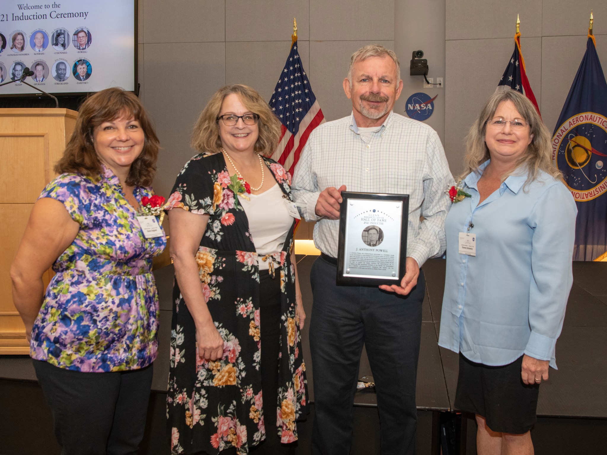 Three women and man posing with plaque.