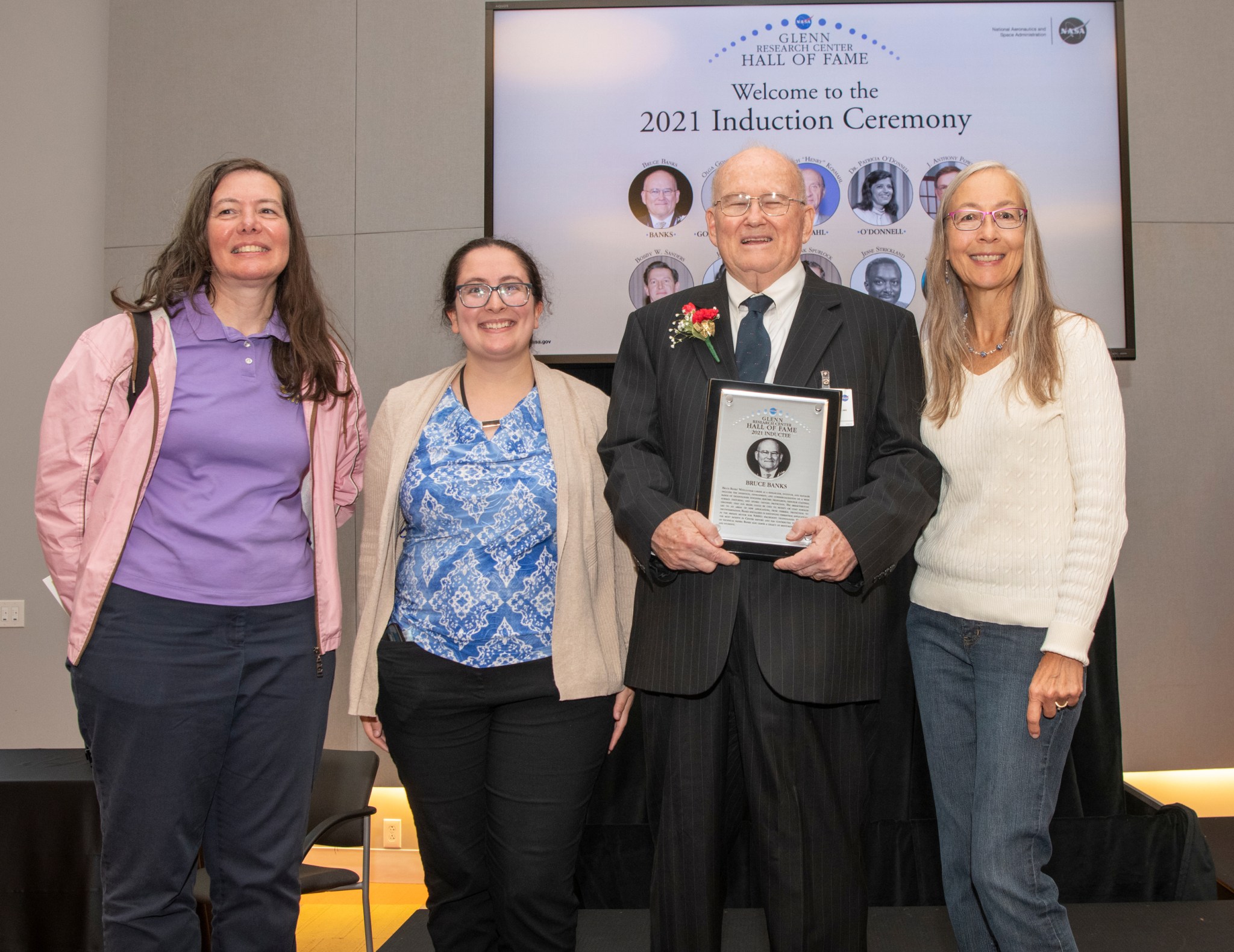 Three women and man posing with plaque.