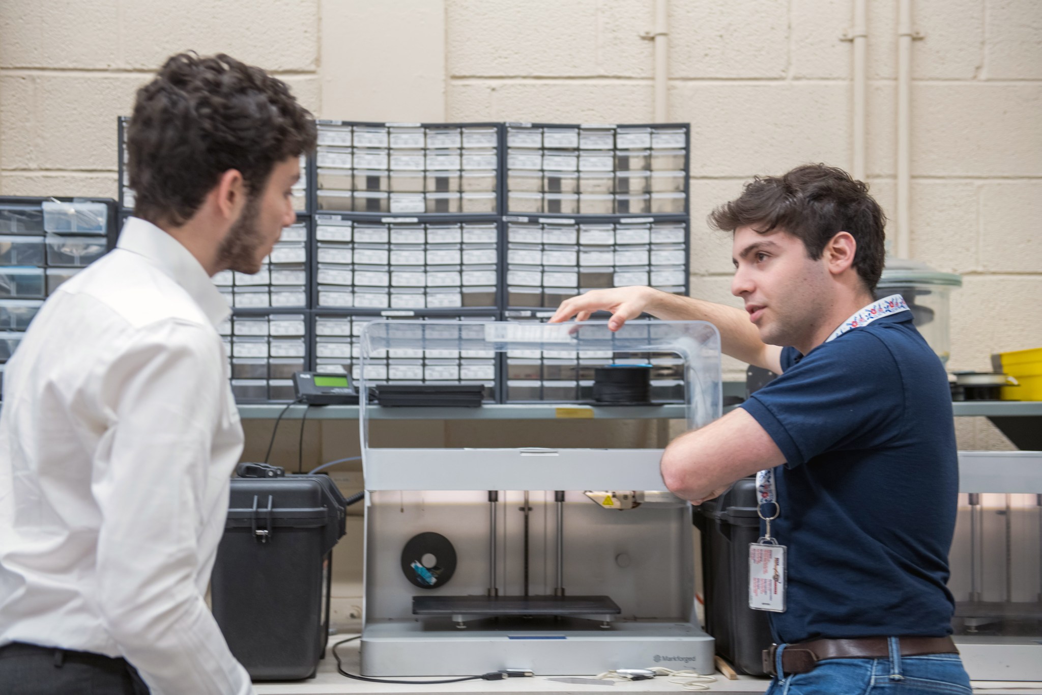 A student, left, looks at a 3D printer on a table as a NASA employee, right, explains how it works and why it is important to research.