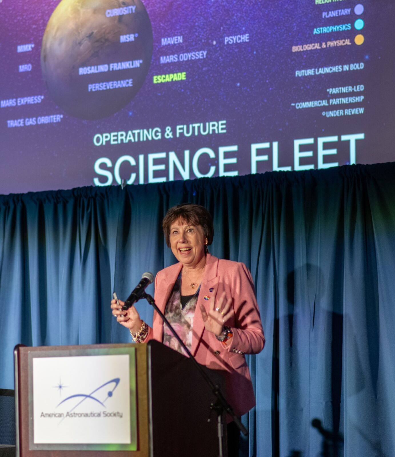 mid shot of Dr. Nicola Fox at a podium with a "SCIENCE FLEET" graphic displaying on a screen above her head