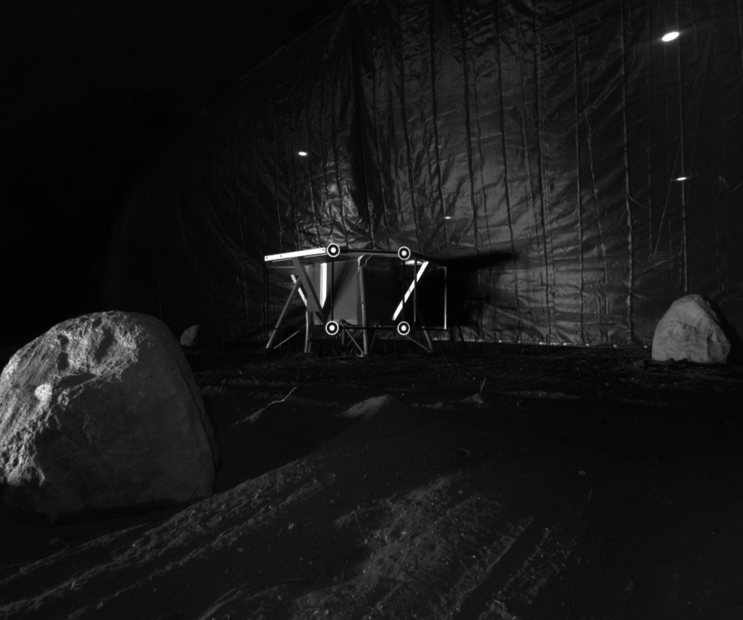 A photo taken from the ISRU Pilot Excavator as it is tested in a blacked out facility with minimal lighting that mimics the harsh, feature-less terrain of the Moon.