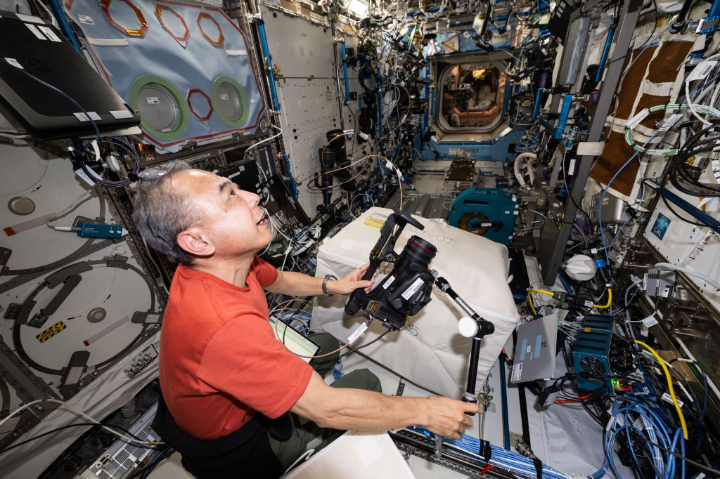 Expedition 70 Flight Engineer and JAXA (Japan Aerospace Exploration Agency) astronaut Satoshi Furukawa sets up a video camera that will record him working on a physics experiment inside the International Space Station's Destiny laboratory module.
