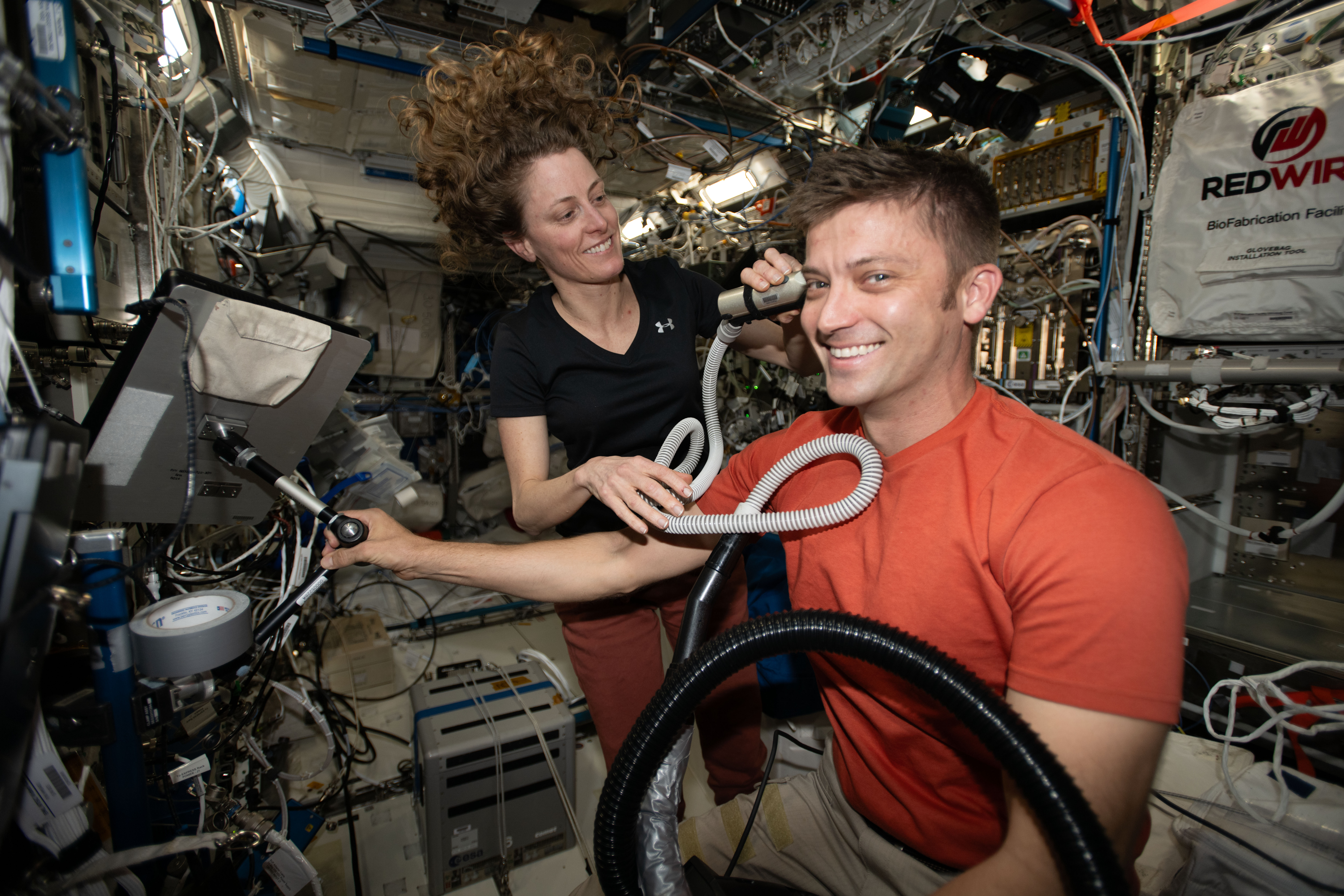 Expedition 70 Flight Engineers Loral O'Hara and Matthew Dominick, both NASA astronauts, are pictured as Dominick receives a haircut from O'Hara who is using an electric razor with a vacuum attached that collects the loose hair.