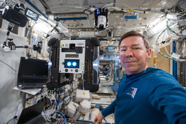 Expedition 70 Flight Engineer and NASA astronaut Mike Barratt shows off an Astrobee robotic free-flyer that will be controlled by student-written code in a competition to inspire the next generation of scientists, engineers, and explorers.