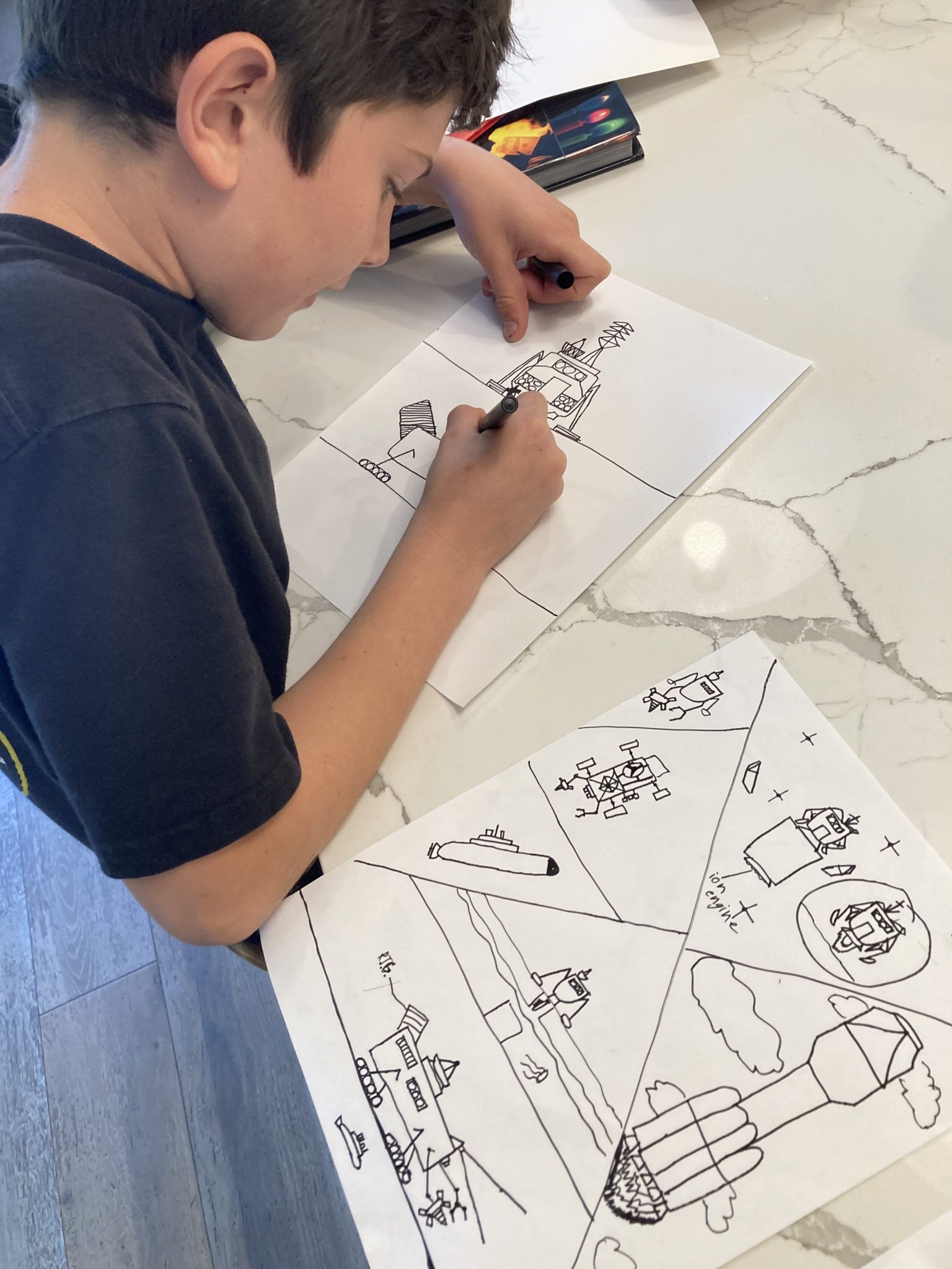 A young boy draws imagined spacecraft on paper.