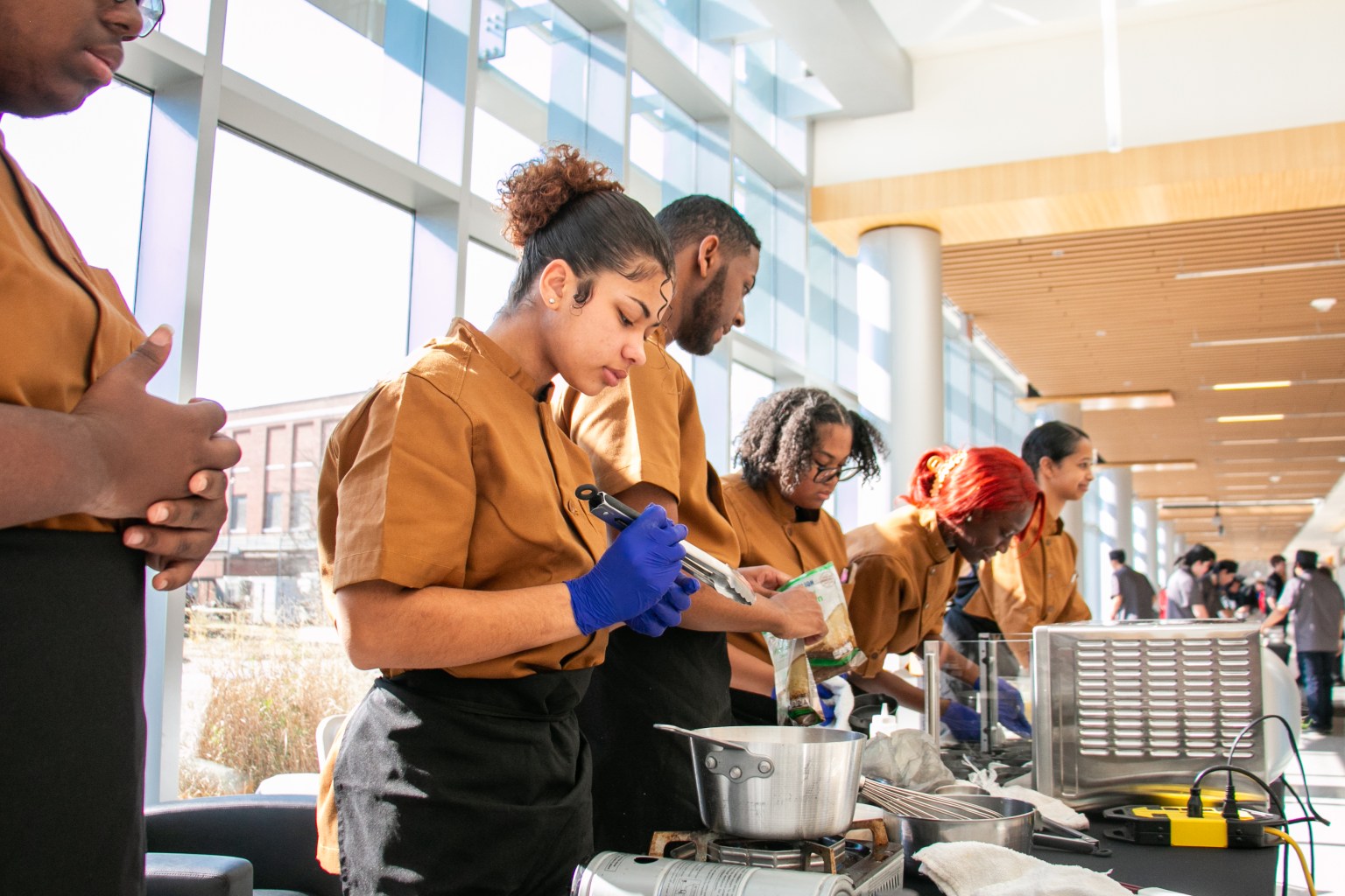 High school students in deep orange chef jackets stand above pots, pans and other cooking equipment as they prepare their savory breakfast meal for the NASA HUNCH Culinary Challenge.