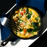 A cooked egg frittata with colorful vegetables sits in a small black cast iron and serving dish after being tasted by the judges.