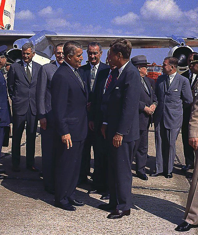 Group of men standing on tarmac.