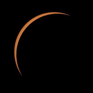 In the darkness of the sky, the Sun appears as a thin crescent of orange gold. The Moon blocks most of it from view.