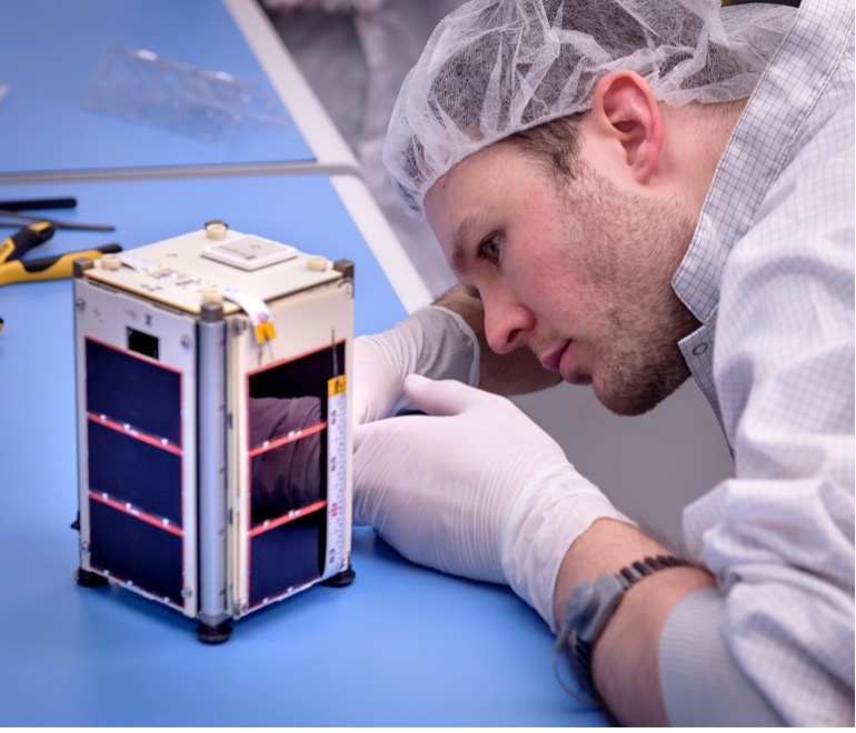 A person in a lab reaches into a small box-like structure on a table.