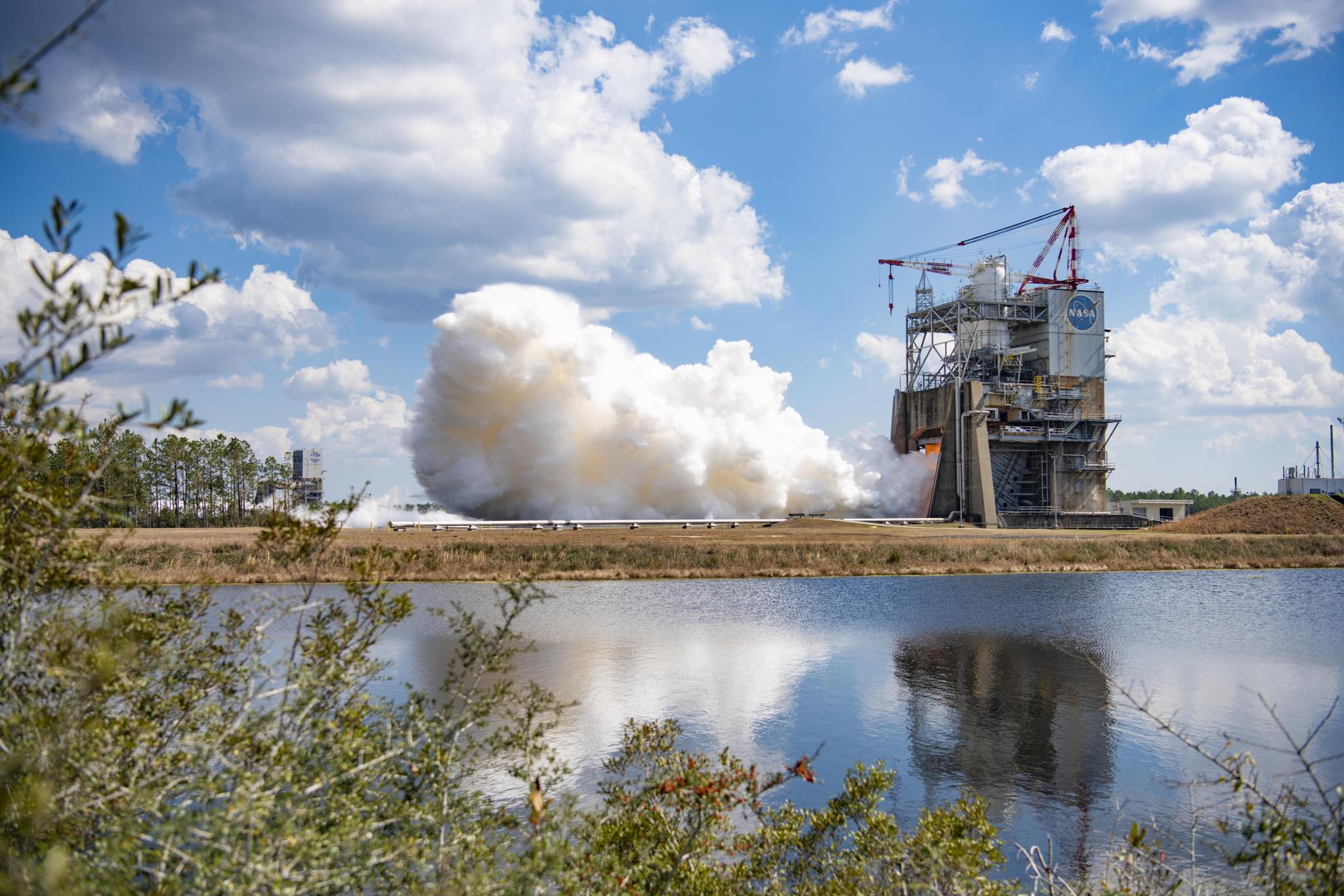 vapor clouds erupt from a RS-25 hot fire from across the water