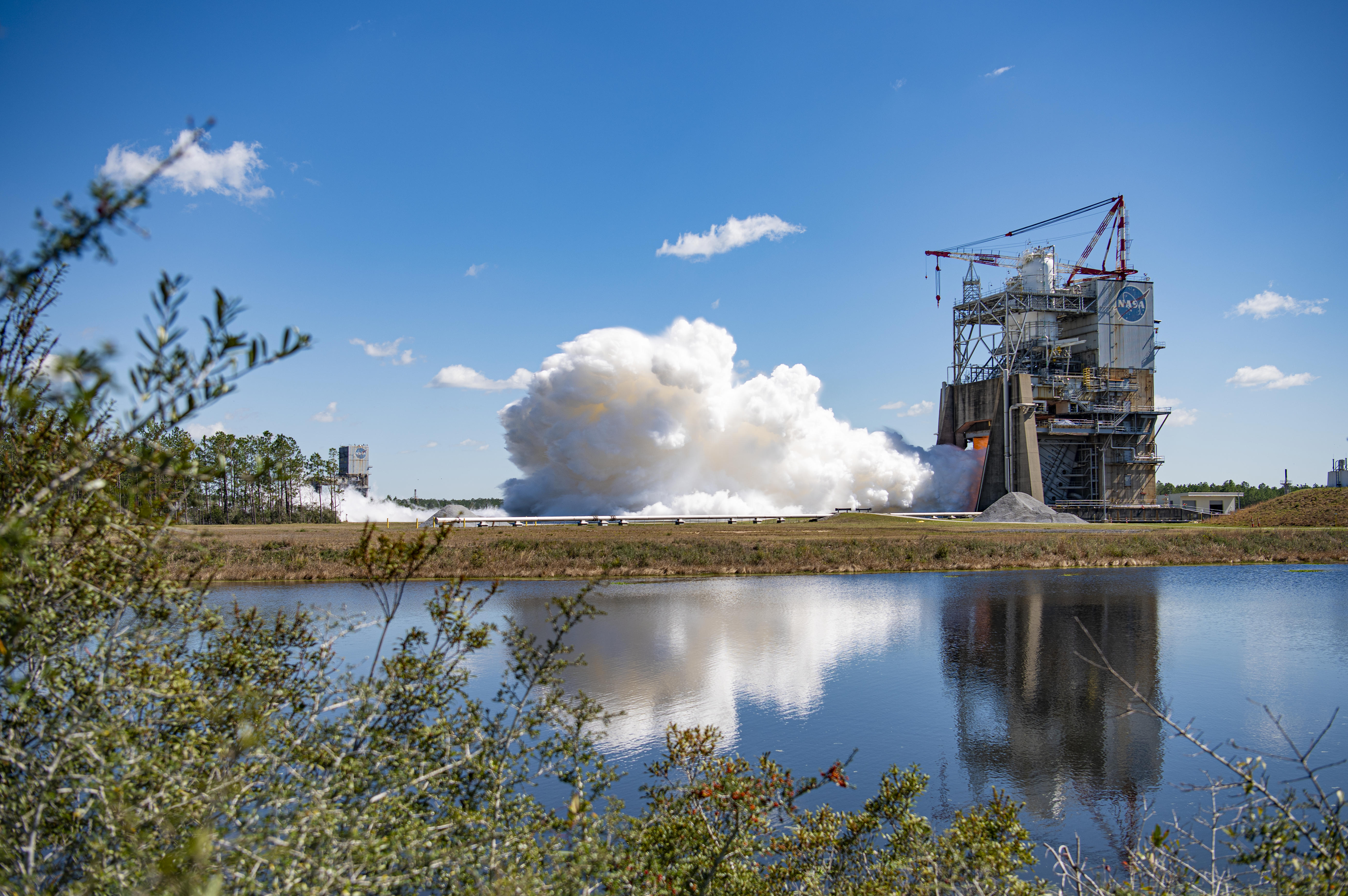full-duration RS-25 engine hot fire is visible in the background of the image