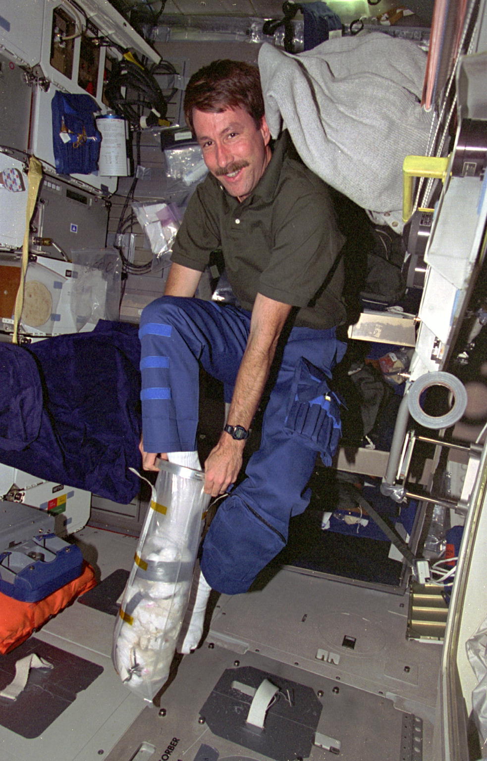 an astronaut pushing trash down into a bag with his foot