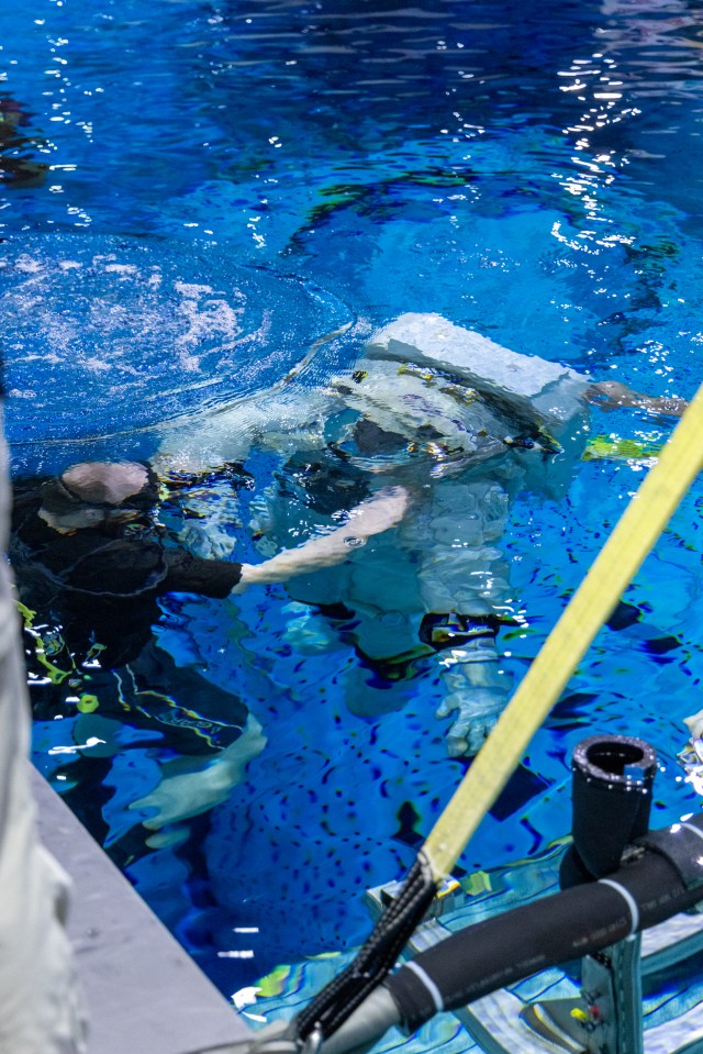 Axiom Space's AxEMU (Axiom Extravehicular Mobility Unit) spacesuit underwater during testing of its pressure garment system at NASA Johnson's Neutral Buoyancy Laboratory. The white spacesuit is seen underwater alongside a scuba diver.