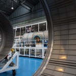 In the background, a large space station module for Gateway in a facility ringed by inspection scaffolding. In the foreground, large gray rings.