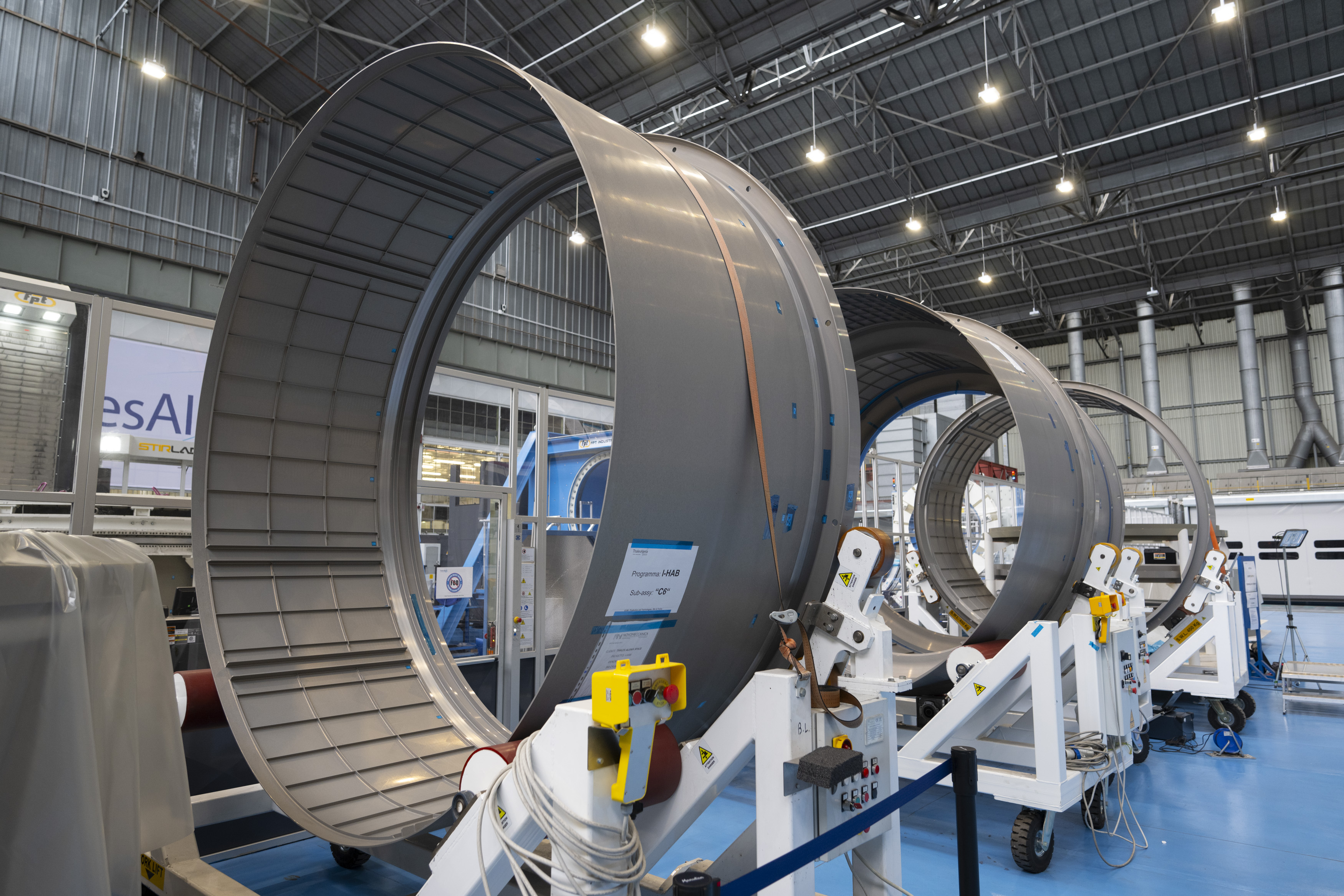 Industrial facility with large cylindrical metallic rings supported by frameworks, equipped with electronic control units.