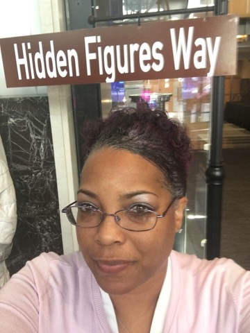 closeup of Shawnta Ball's face with a brown "Hidden Figures Way" street sign above her head